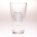 A clear glass drinking tumbler with black printed text reading 'Aquarius' and a poem associated with the Aquarius zodiac sign, shown on a plain light background.