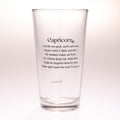 A clear glass drinking tumbler with black printed text reading 'Capricorn' and a poem beneath it, shown on a plain light background.