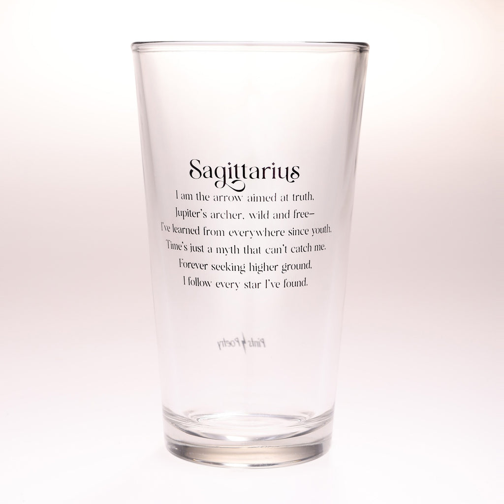 A clear glass pint glass with black printed text on the front reading 'Sagittarius' followed by a descriptive quote, photographed against a clean white background.