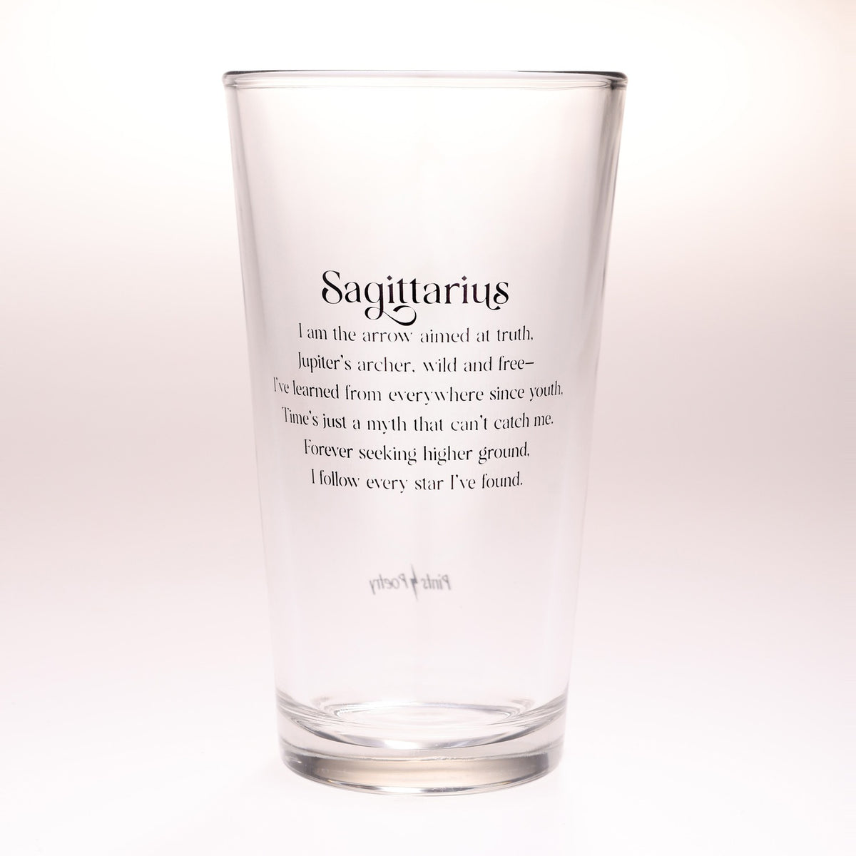 A clear glass pint glass with black printed text on the front reading 'Sagittarius' followed by a descriptive quote, photographed against a clean white background.
