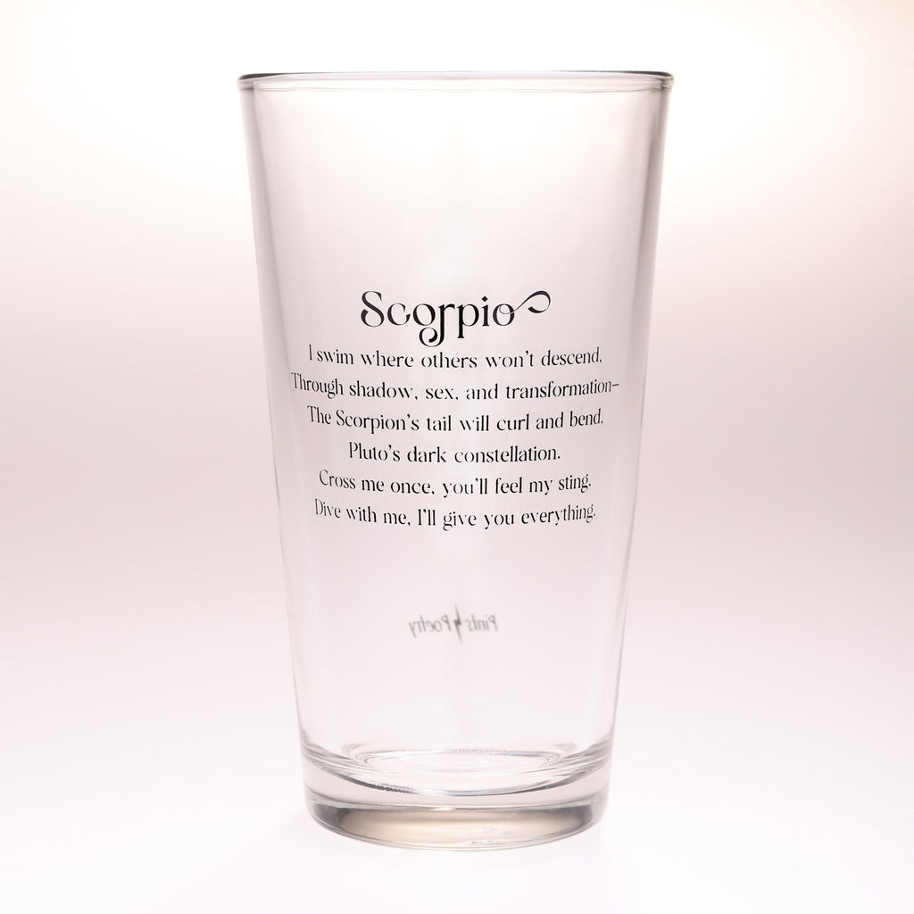 A clear glass pint glass with black printed text featuring the Scorpio zodiac sign and its astrological description, set against a plain white background.