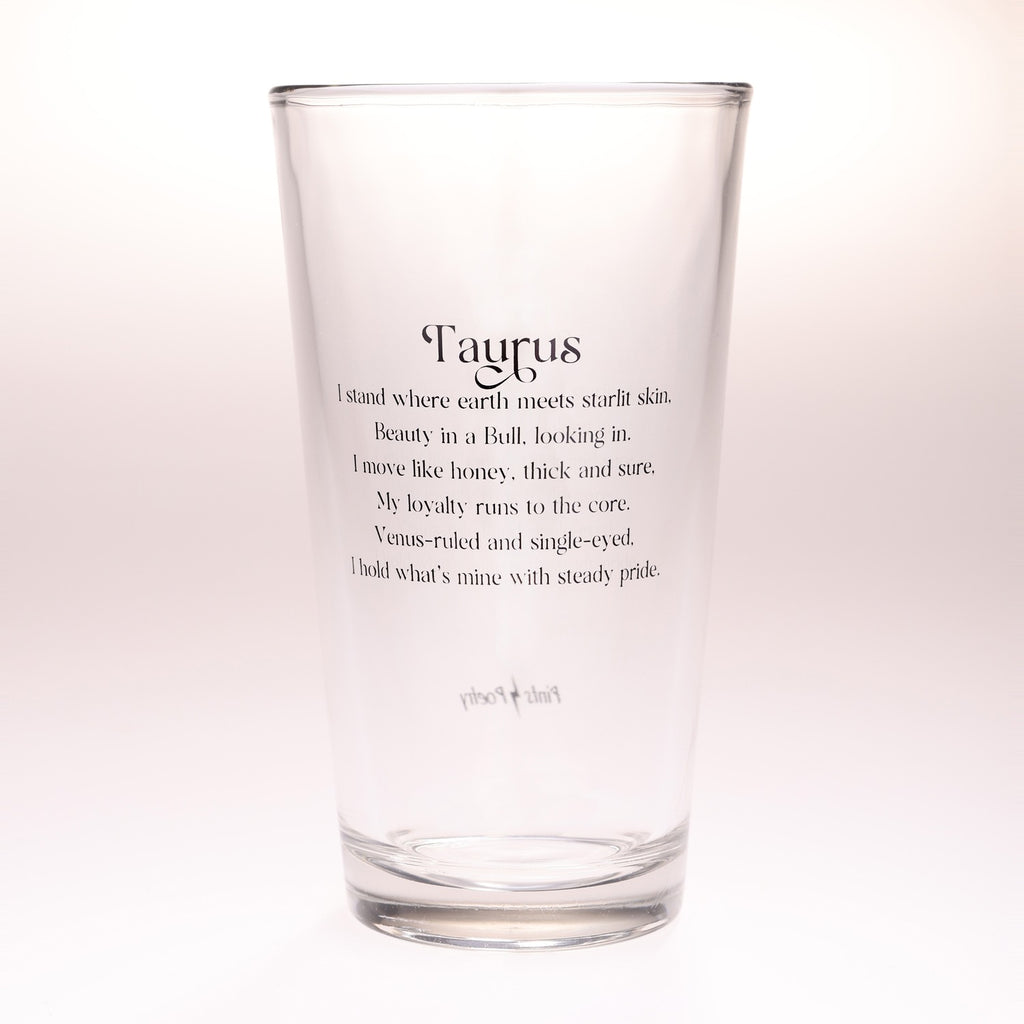 A clear glass drinking tumbler with black printed text reading 'Taurus' and a poem about the zodiac sign, photographed against a plain light background.