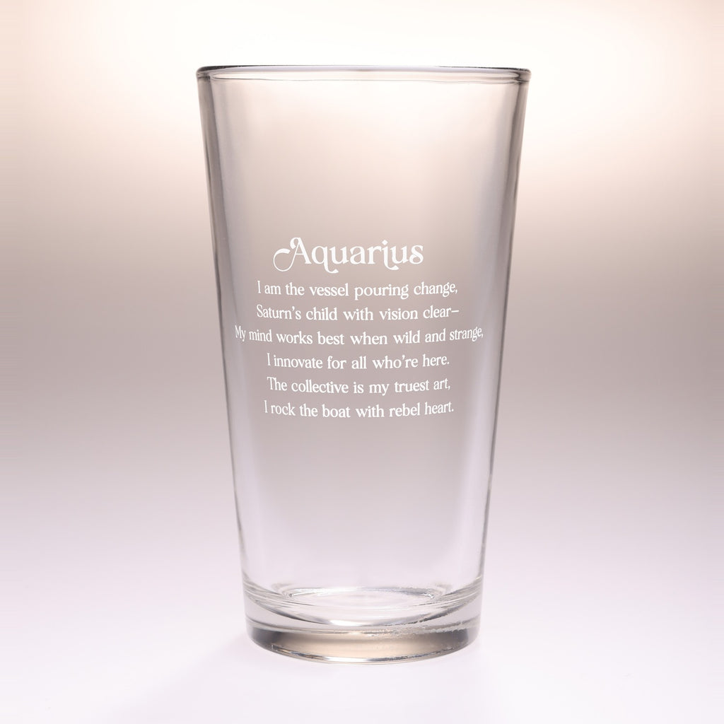 A clear glass drinking tumbler with etched Aquarius zodiac text and quote on the front, photographed against a soft beige-to-white gradient background.