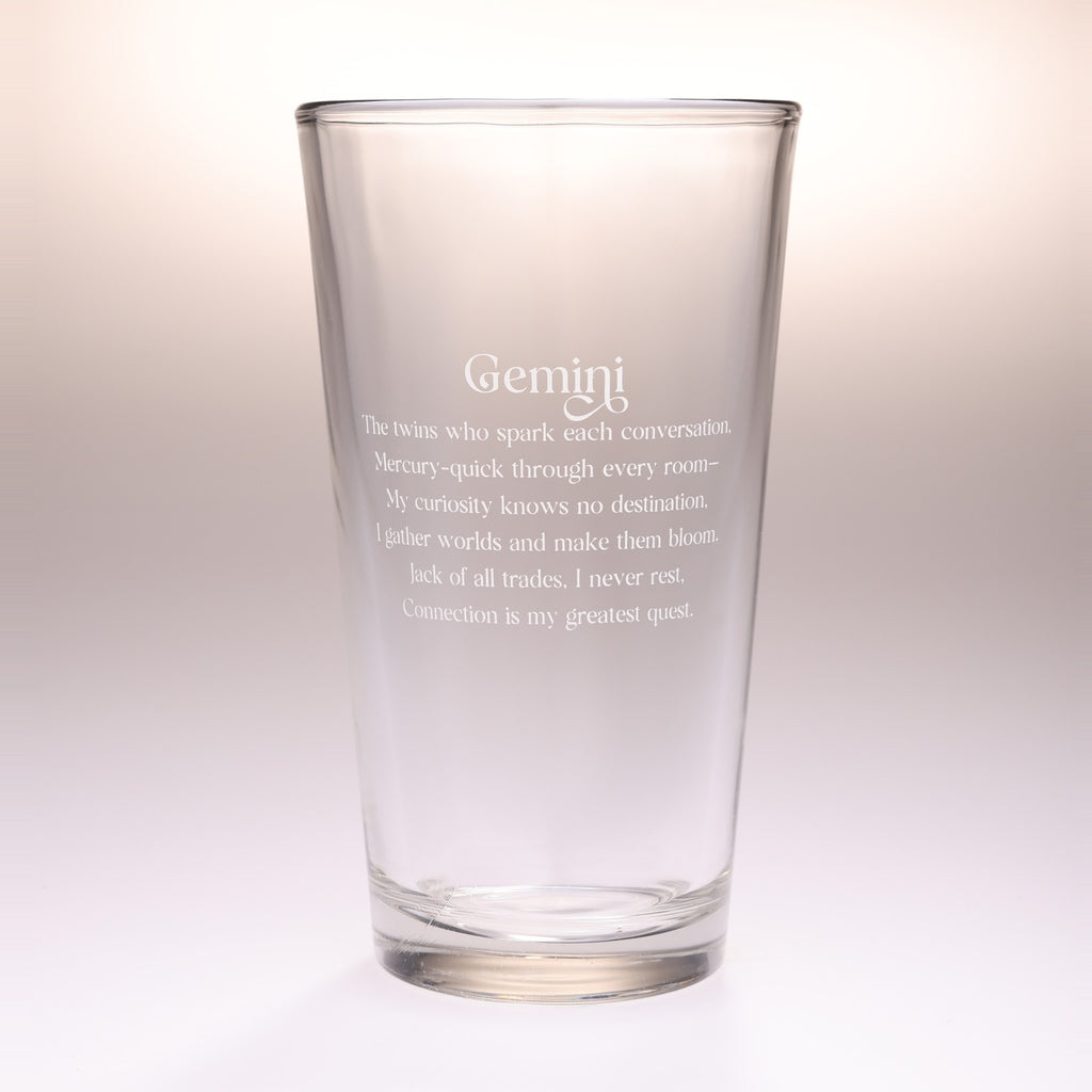 A clear glass drinking tumbler with etched Gemini zodiac text on the front, shown against a soft beige gradient background.