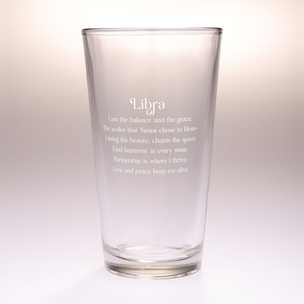 A clear glass drinking tumbler with etched white text reading 'Libra' and a poem associated with Libra, shown on a soft light gray to white gradient background.