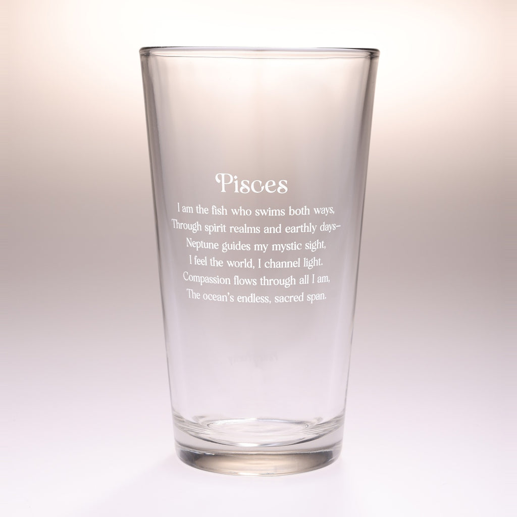 A clear glass pint glass with white printed text reading 'Pisces' followed by a zodiac-related poem, shown on a clean light gray to white studio background.