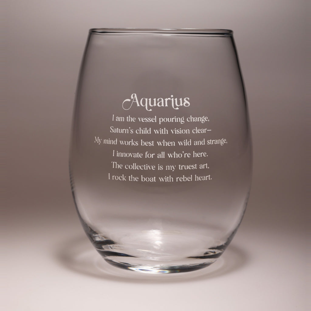 A clear stemless wine glass with frosted white text that reads 'Aquarius' followed by a poem, shown on a neutral gray studio background.