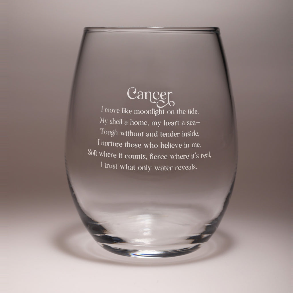 A clear stemless wine glass with white printed text reading 'Cancer' and a poem about moonlight and a sea, shown on a neutral gray studio background.