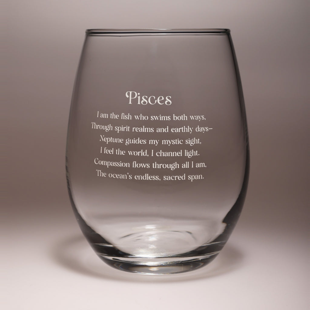 A clear stemless wine glass with frosted etched text reading 'Pisces' and a poem below, shown on a neutral gray studio background.