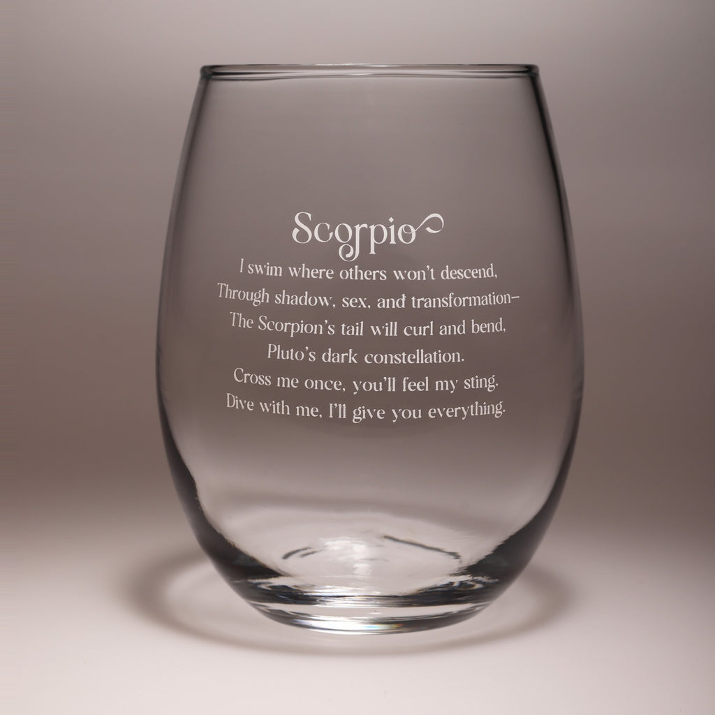A clear stemless wine glass with etched Scorpio zodiac text and a poem printed on the front, set against a neutral gray studio background.