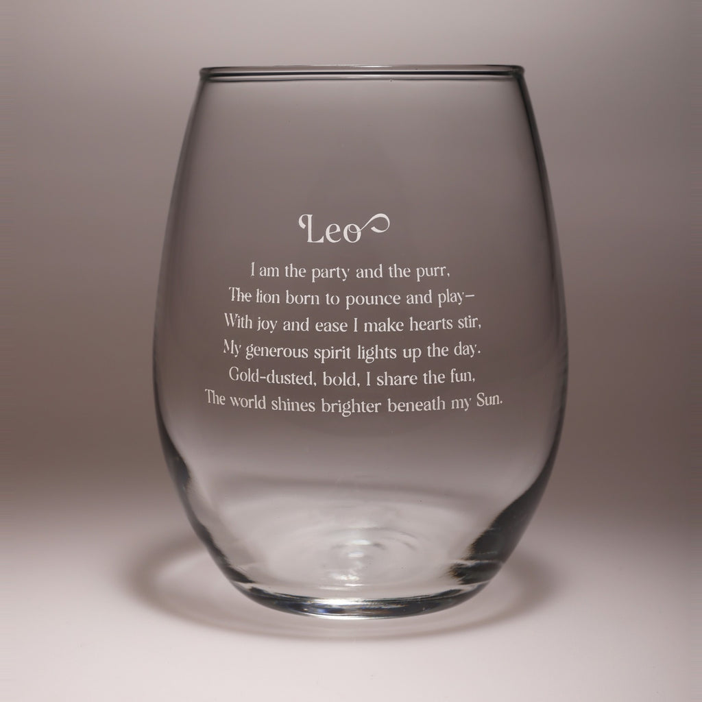 A clear stemless wine glass with etched Leo zodiac sign text and a poem printed on the front, shown against a neutral gray studio background.