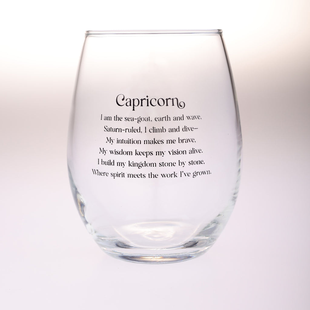 A clear stemless wine glass with black printed text reading 'Capricorn' and a descriptive astrological quote, shown against a soft white background.