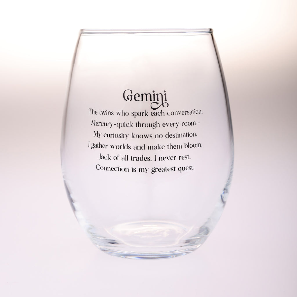 A clear stemless wine glass with black printed text reading 'Gemini' and a descriptive quote about Gemini twins, shown on a soft white background.