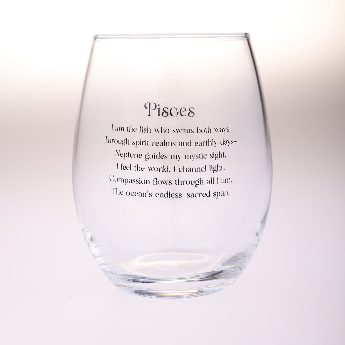 A clear stemless wine glass with black printed text reading 'Pisces' followed by a poem about the Pisces zodiac sign, shown on a plain light background.