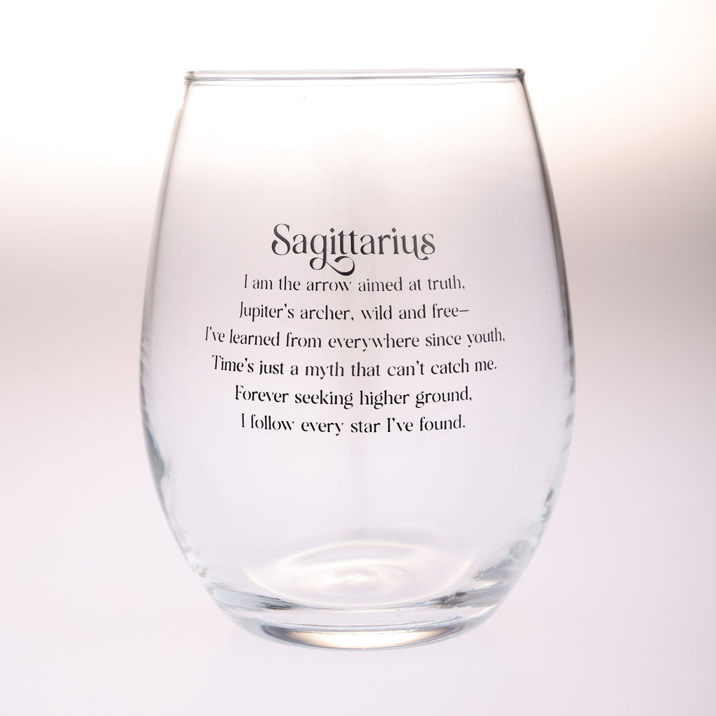 A clear stemless wine glass with black printed text reading 'Sagittarius' and a descriptive quote about being an arrow aimed at truth, photographed against a soft white background.