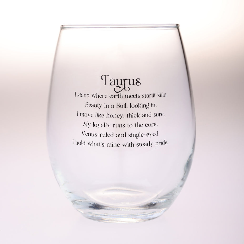 A clear stemless wine glass with black printed text reading 'Taurus' and a poem about the zodiac sign, shown on a soft white background.