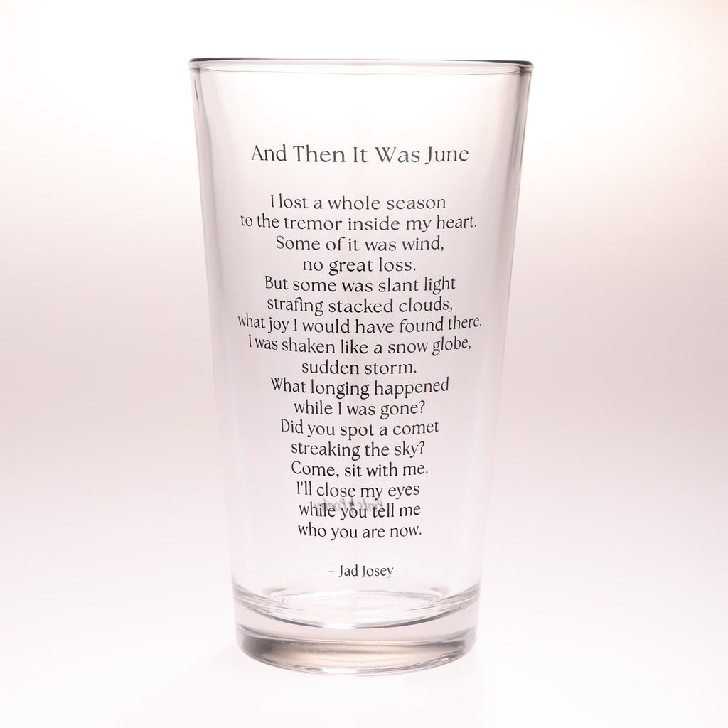 A clear glass drinking tumbler with printed black text of a poem titled 'And Then It Was June' by Jad Josey, shown on a plain white background.