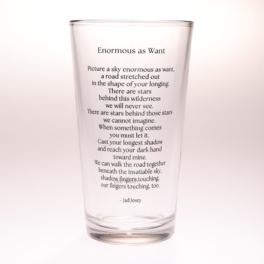 A clear glass drinking tumbler with black printed text of a poem titled 'Enormous as Want' by Jad Josey, shown on a plain white background.