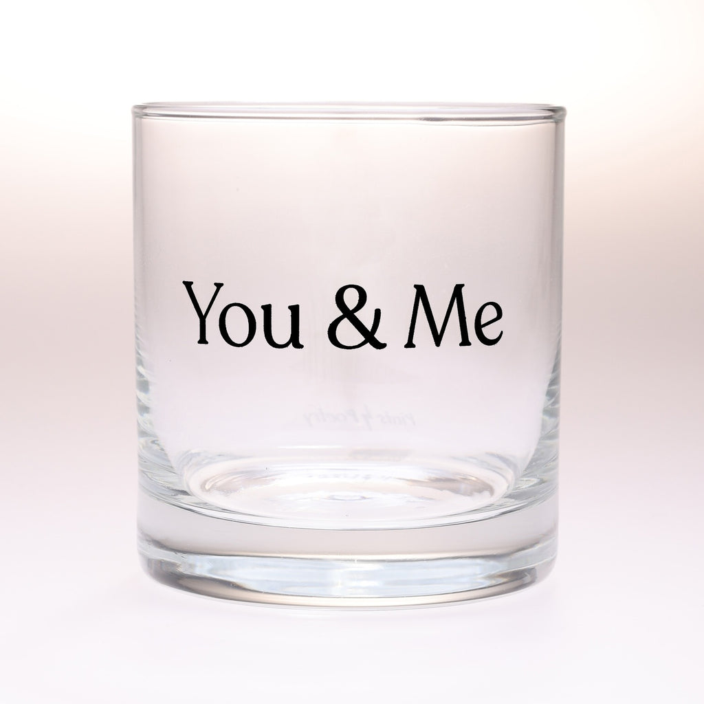 A rocks glass tumbler with the words 'You & Me' printed in black serif font on the front, set against a clean white background.