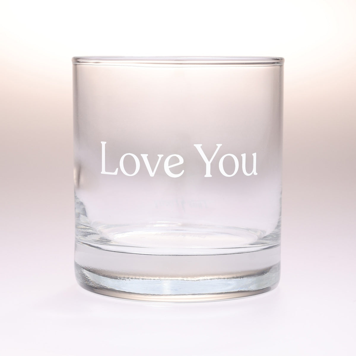 A clear glass rocks tumbler with the words 'Love You' printed in white serif lettering on the front, set against a soft white background.