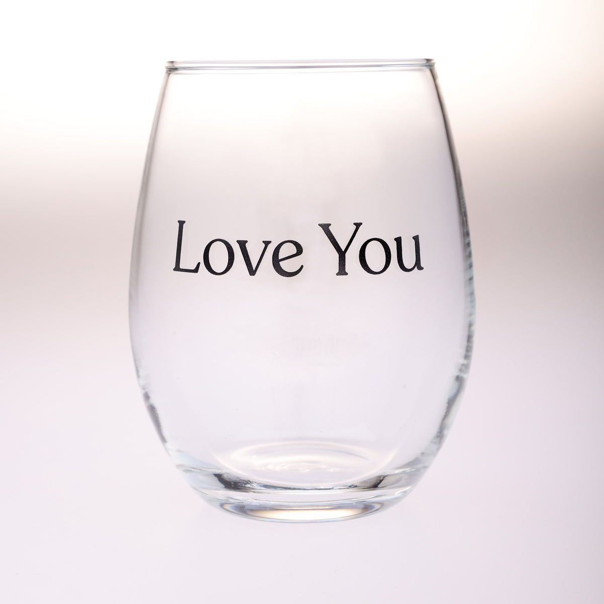 A clear stemless wine glass with the words 'Love You' printed in black serif text on the front, set against a soft white background.